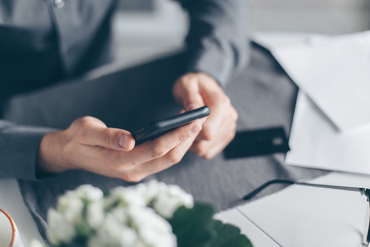 A close-up view of a mans hands using a smartphone with papers on a table.